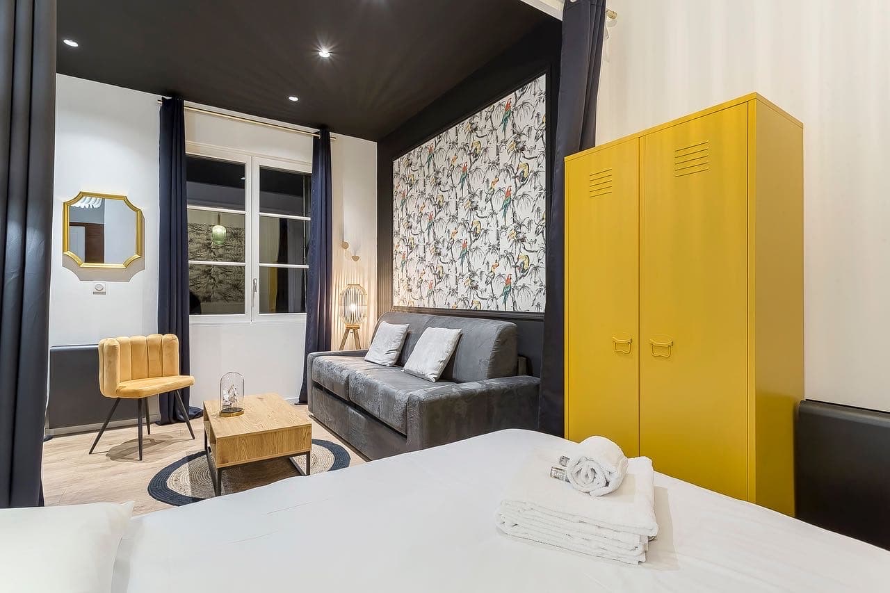 Studio rénové à Bourgoin-Jallieu : plafond noir à spots encastrés, papier peint perroquets derrière le canapé et armoire jaune