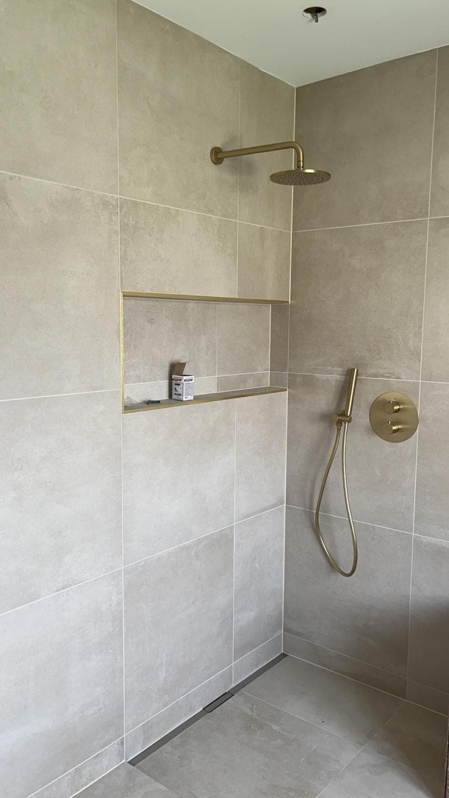 Douche de plain-pied en grands carreaux beige aspect pierre, caniveau linéaire, niche à profilé doré et robinetterie or brossé, Meyzieu