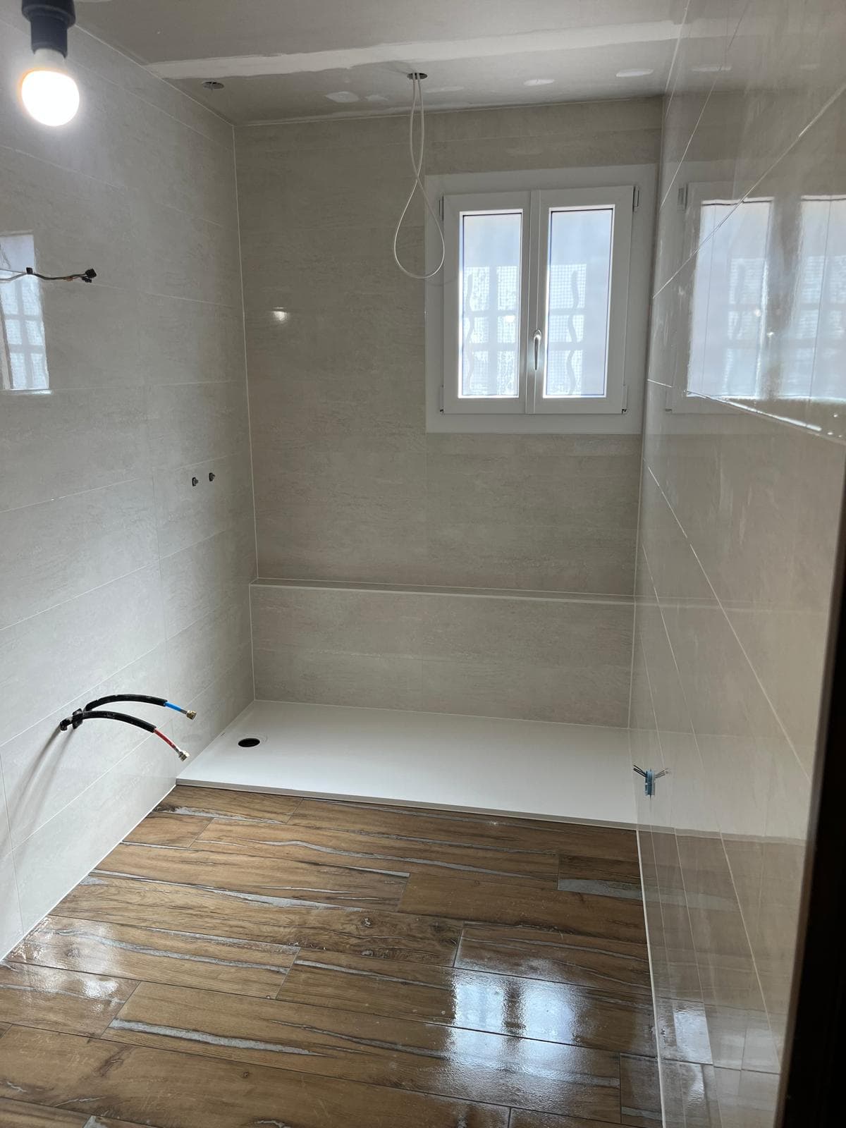 Salle de bain en cours de finition à Jonage : faïence claire posée à l’horizontale, receveur extraplat et sol imitation parquet