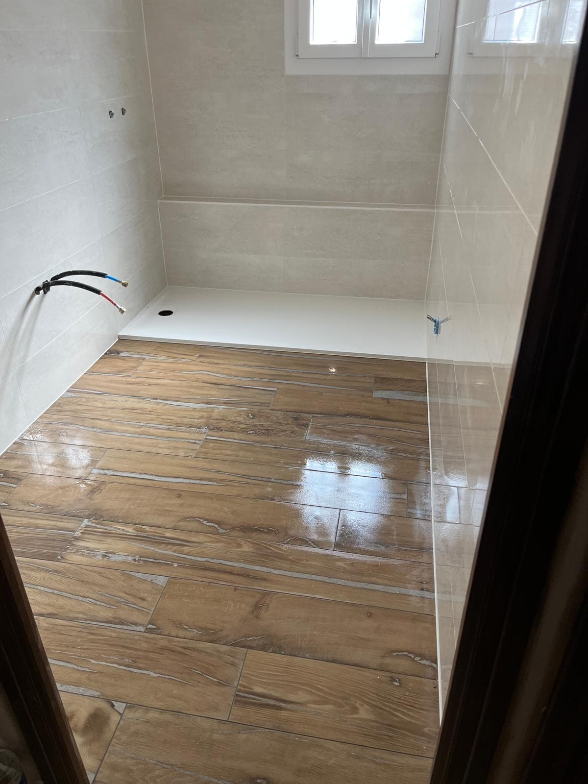 Sol en carrelage imitation parquet posé à joints décalés, encore humide, devant un receveur extraplat blanc, salle de bain à Jonage