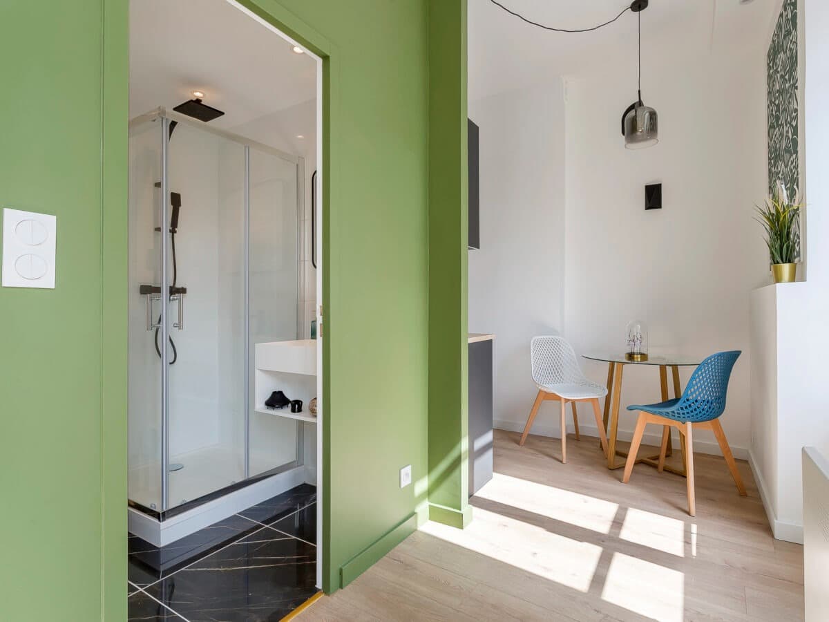 Accès à la salle d’eau par une cloison vert olive : sol carrelé effet marbre noir veiné doré et cabine de douche vitrée, Vaulx-en-Velin