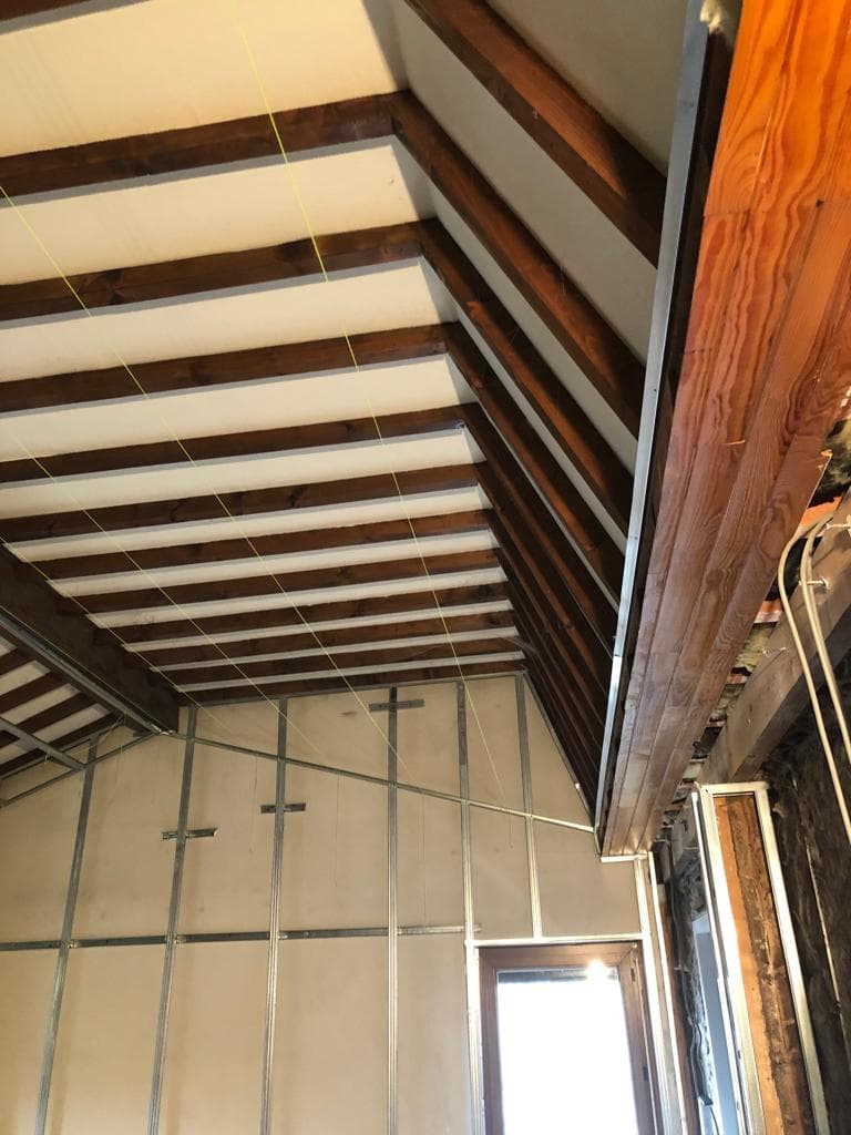 Ossature métallique posée sur un pignon sous toiture, chevrons bois apparents et cordeaux de traçage tendus, chantier à Crémieu